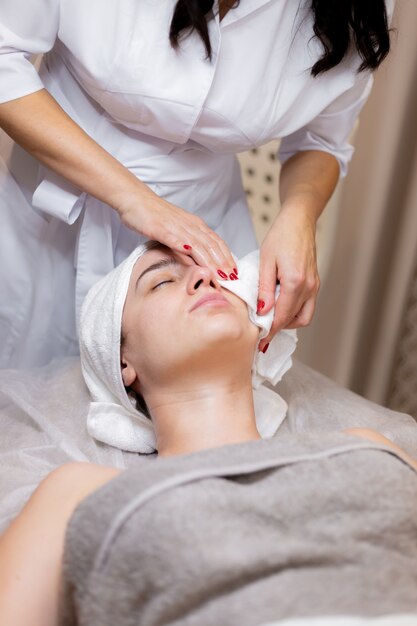 Una joven hermosa se acuesta en la mesa de la esteticista y recibe procedimientos, un ligero masaje facial.