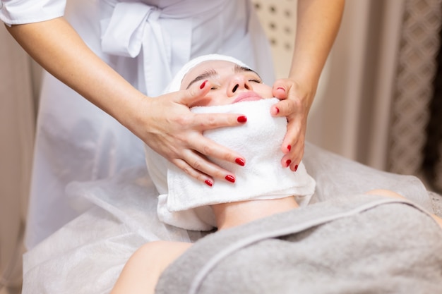 Una joven hermosa se acuesta en la mesa de la esteticista y recibe procedimientos, un ligero masaje facial.