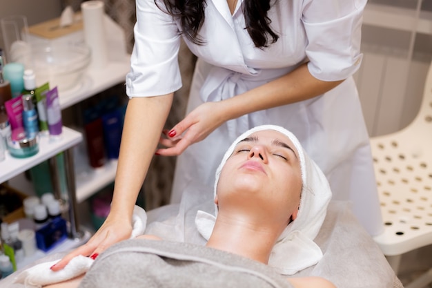 Una joven hermosa se acuesta en la mesa de la esteticista y recibe procedimientos, un ligero masaje facial.