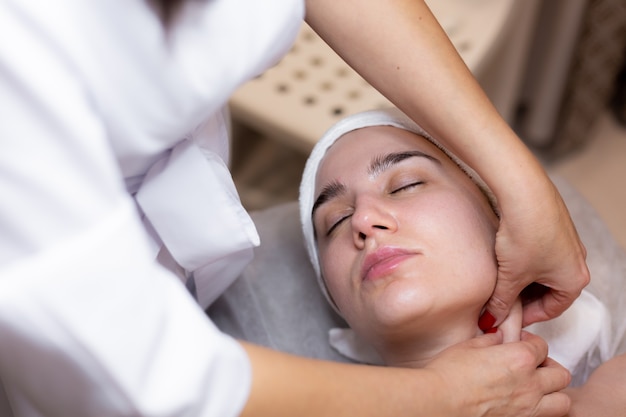 Una joven hermosa se acuesta en la mesa de la esteticista y recibe procedimientos, un ligero masaje facial.