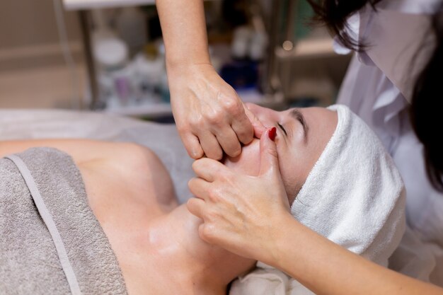 Una joven hermosa se acuesta en la mesa de la esteticista y recibe procedimientos, un ligero masaje facial.