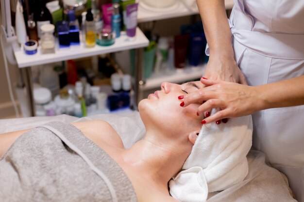 Una joven hermosa se acuesta en la mesa de la esteticista y recibe procedimientos, un ligero masaje facial.