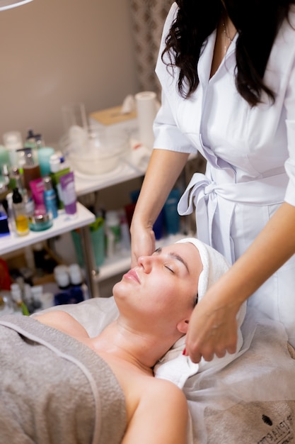 Una joven hermosa se acuesta en la mesa de la esteticista y recibe procedimientos, un ligero masaje facial.