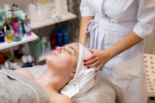 Una joven hermosa se acuesta en la mesa de la esteticista y recibe procedimientos, un ligero masaje facial.