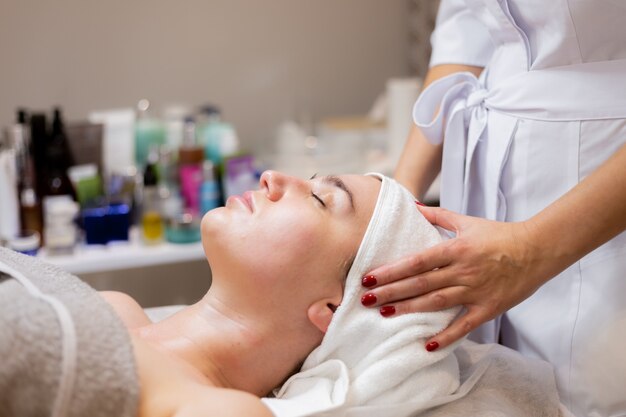 Una joven hermosa se acuesta en la mesa de la esteticista y recibe procedimientos, un ligero masaje facial.