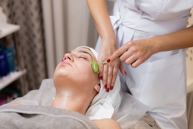 Una joven hermosa se acuesta en la mesa de la esteticista y recibe procedimientos, un ligero masaje facial.