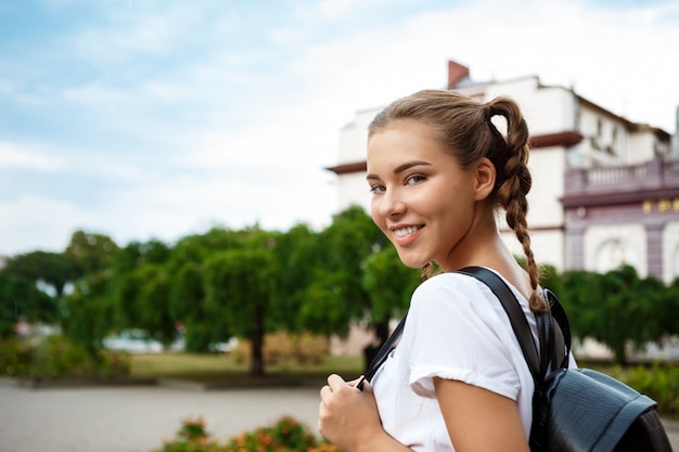 Foto gratuita joven hermosa alegre estudiante sonriente, sosteniendo carpetas al aire libre