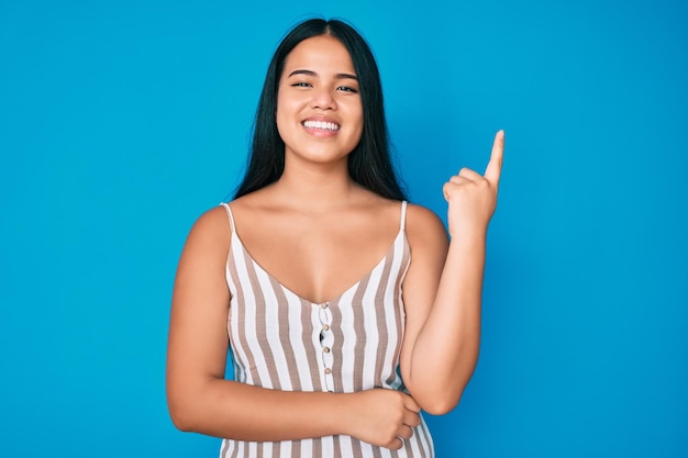 Joven hermosa chica asiática con ropa informal con una gran sonrisa en la cara, señalando con la mano y el dedo hacia un lado mirando la cámara.