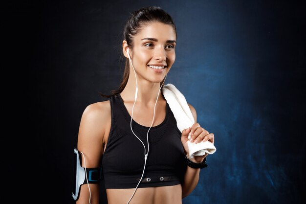 Joven hermosa chica deportiva escuchando música sobre la pared oscura.