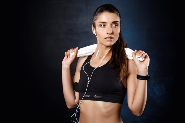 Joven hermosa chica deportiva escuchando música sobre la pared oscura.