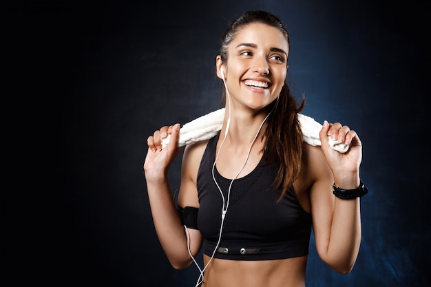 Joven hermosa chica deportiva escuchando música sobre la pared oscura.