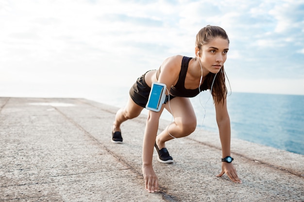 Joven hermosa chica deportiva preparándose para correr sobre la playa.