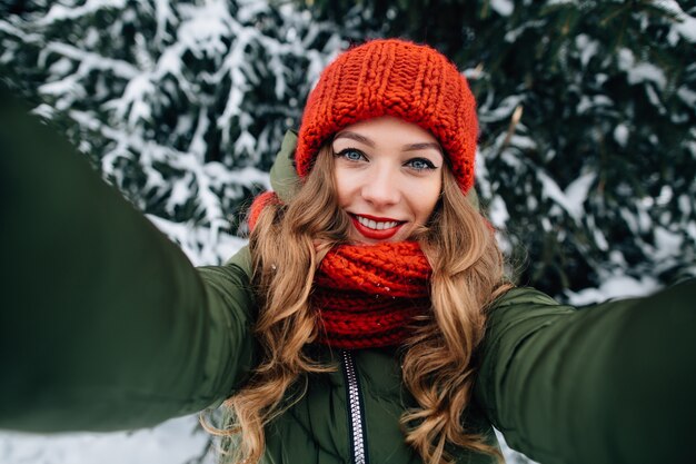 Joven hermosa chica feliz en invierno rojo sombrero hecho punto y bufanda toma selfie