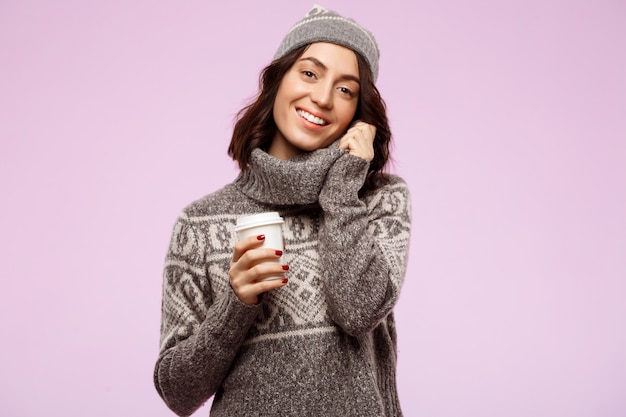 Joven hermosa chica morena sonriendo sosteniendo café sobre la pared de luz