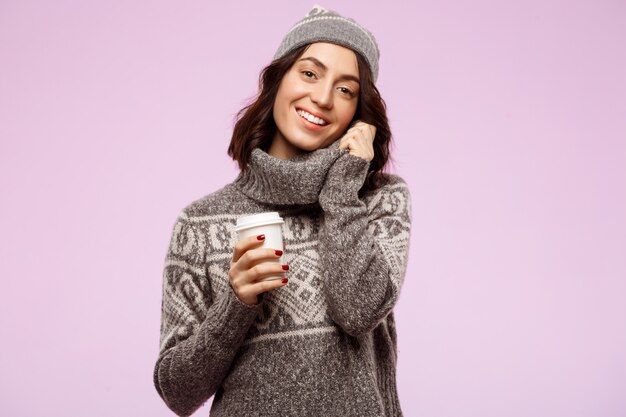 Joven hermosa chica morena sonriendo sosteniendo café sobre la pared de luz