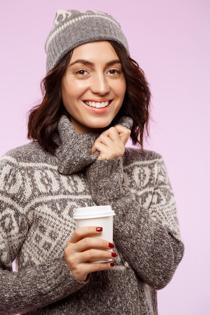 Joven hermosa chica morena sonriendo sosteniendo café sobre la pared de luz