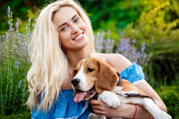 Joven hermosa chica rubia caminando, jugando con el perro beagle en el parque.