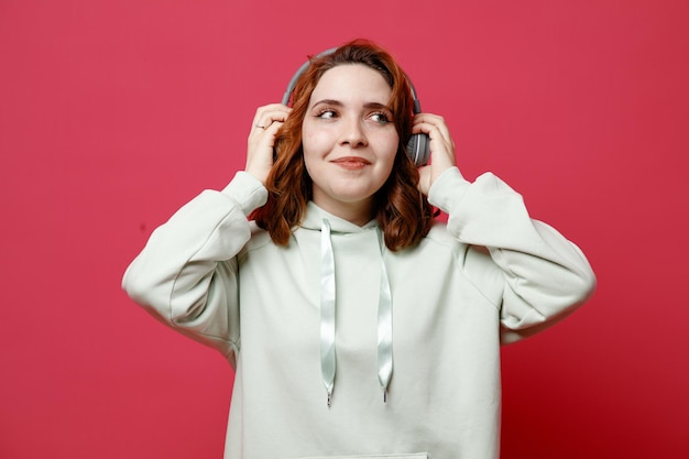 Una joven hermosa y complacida con suéter blanco usando audífonos aislados en un fondo rosa