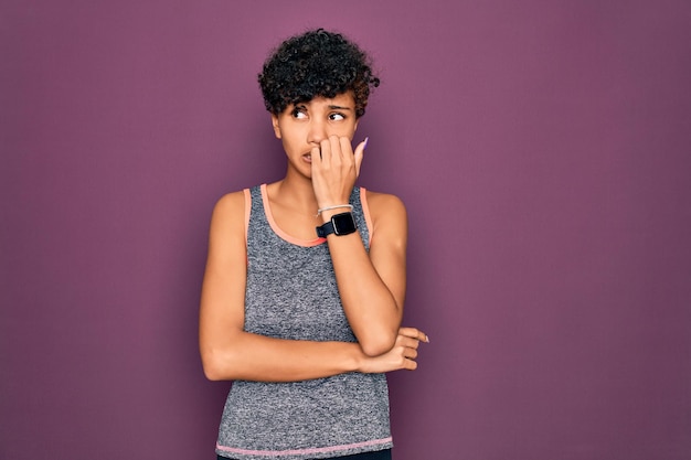 Joven y hermosa deportista afroamericana haciendo ejercicio usando ropa deportiva luciendo estresada y nerviosa con las manos en la boca mordiéndose las uñas Problema de ansiedad