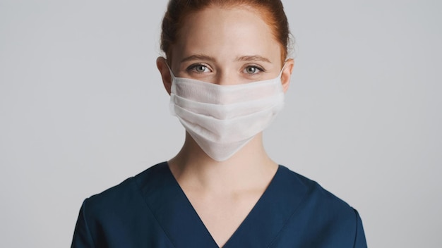 Joven y hermosa doctora con máscara médica mirando felizmente a la cámara sobre fondo blanco Concepto de seguridad