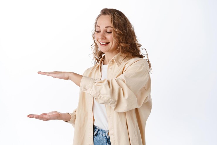 Foto gratuito joven y hermosa estudiante rubia sosteniendo un espacio de copia vacío entre las manos mostrando el logotipo o el producto de gran tamaño sonriendo y complacida con el fondo blanco del artículo