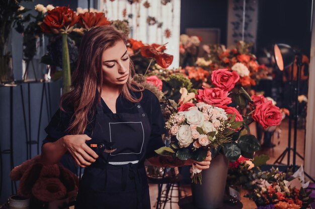 Una joven y hermosa florista está trabajando en un ramo en su floristería.