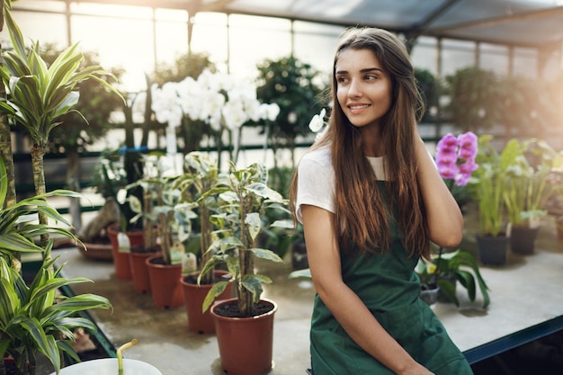 Joven y hermosa jardinera sentada en un invernadero