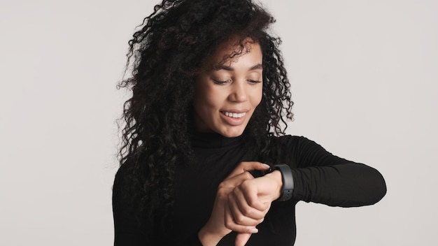 Joven hermosa mujer afro que parece feliz respondiendo mensajes usando un reloj inteligente aislado en fondo blanco