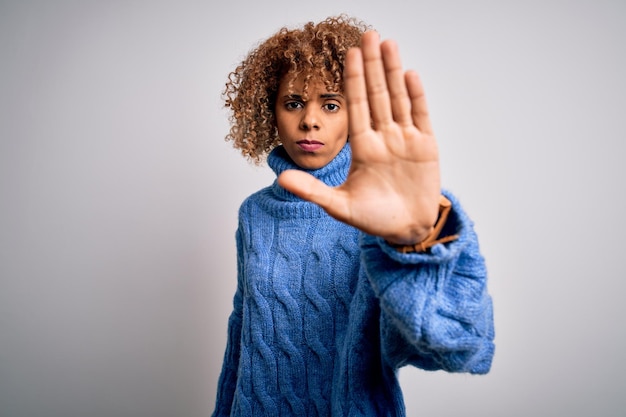 Foto gratuita joven hermosa mujer afroamericana con suéter de cuello alto sobre fondo blanco que deja de cantar con la palma de la mano expresión de advertencia con gesto negativo y serio en la cara