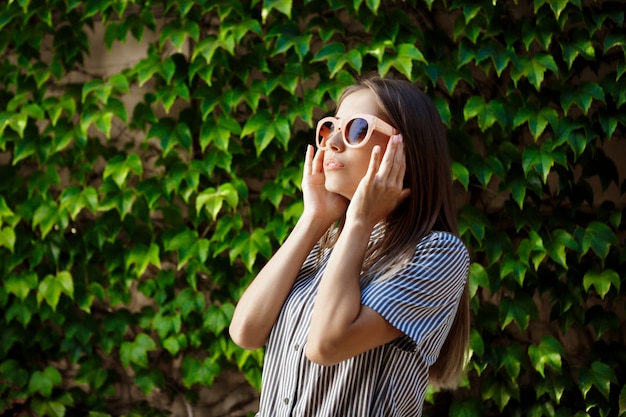 Joven hermosa mujer alegre en gafas de sol caminando por la ciudad, sonriendo.