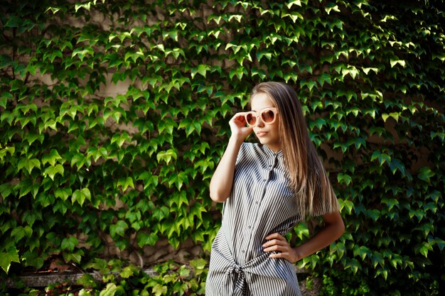 Joven hermosa mujer alegre en gafas de sol caminando por la ciudad, sonriendo.