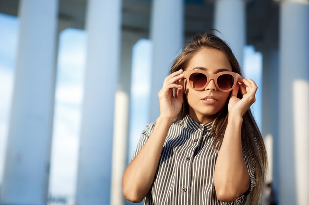 Joven hermosa mujer alegre en gafas de sol caminando por la ciudad.