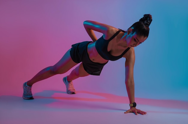 Joven hermosa mujer asiática con cuerpo atlético haciendo flexiones en el moderno gimnasio