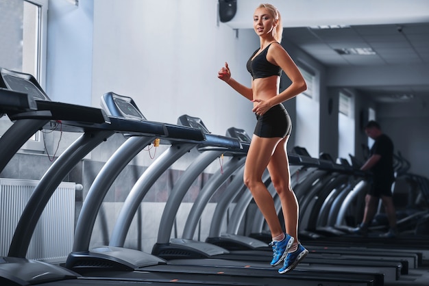 Joven hermosa mujer atlética corriendo en una cinta en el gimnasio