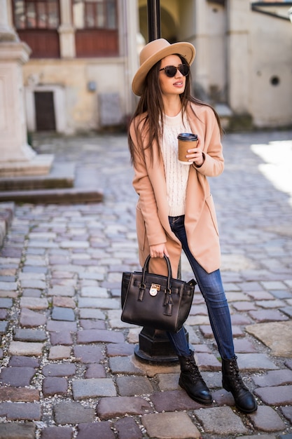 Foto gratuita joven hermosa mujer bonita caminando por la calle con bolso y taza de café.