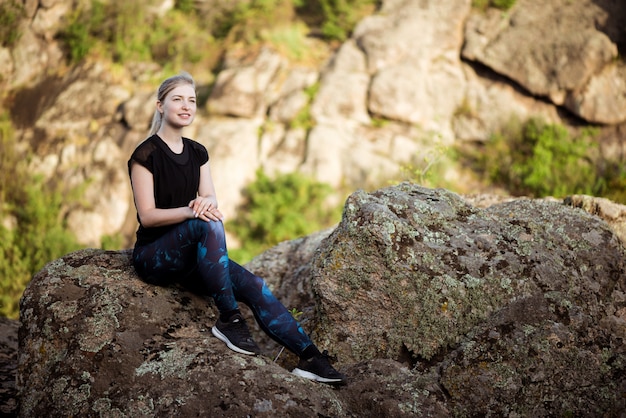 Joven hermosa mujer deportiva sonriendo, sentado en la roca en el cañón