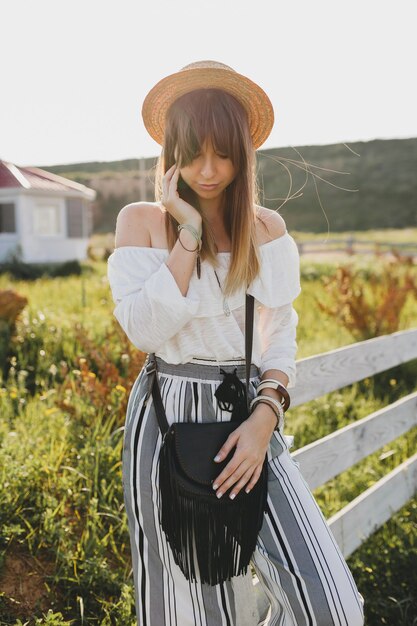 Joven hermosa mujer elegante, tendencia de moda primavera verano, estilo boho, sombrero de paja, fin de semana de campo, soleado, bolso negro