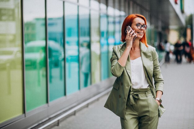 Joven hermosa mujer exitosa en traje verde hablando por teléfono