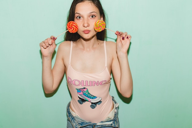 Foto gratuita joven hermosa mujer hipster posando contra la pared azul, sosteniendo lolly pop candy