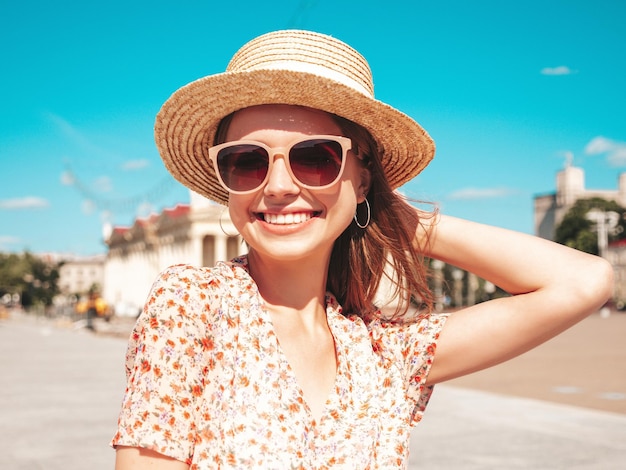 Joven hermosa mujer hipster sonriente en ropa de verano de moda Mujer sexy despreocupada posando en el fondo de la calle al atardecer Modelo positivo al aire libre Alegre y feliz con gafas de sol y sombrero