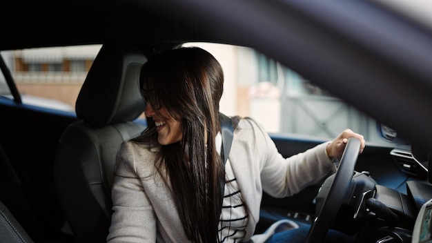 Joven hermosa mujer hispana sonriendo confiada conduciendo un auto en la calle