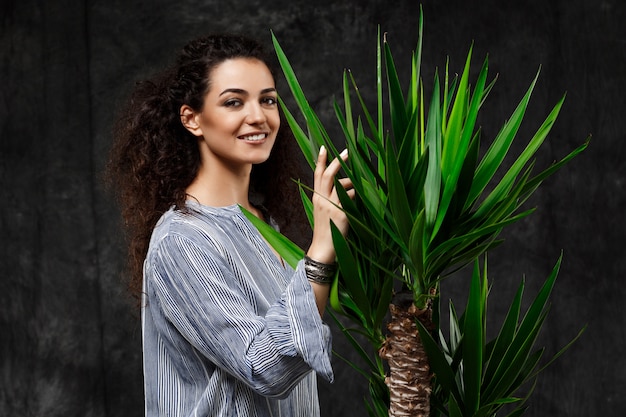 Foto gratuita joven hermosa mujer morena en plantas tropicales sobre pared gris