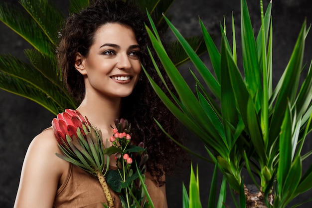 Joven hermosa mujer morena en plantas tropicales sobre superficie gris