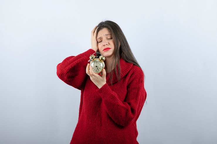 Foto gratuito joven hermosa mujer morena sosteniendo un reloj de alarma de pie sobre fondo blanco.