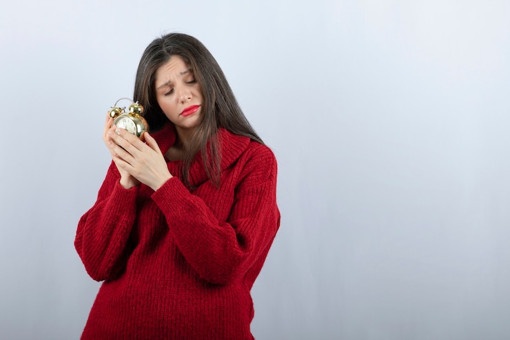 Foto gratuito joven hermosa mujer morena sosteniendo un reloj de alarma de pie sobre fondo blanco.