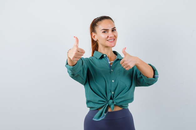 Foto gratuita joven hermosa mujer mostrando los pulgares para arriba en camisa verde y mirando alegre, vista frontal.