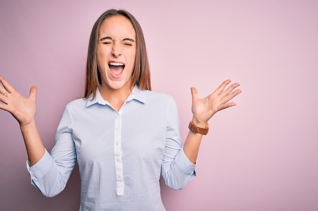 Foto gratuita joven y hermosa mujer de negocios con pantalones elegante sobre un fondo rosa aislado celebrando loco y loco por el éxito con los brazos levantados y los ojos cerrados gritando emocionado concepto de ganador