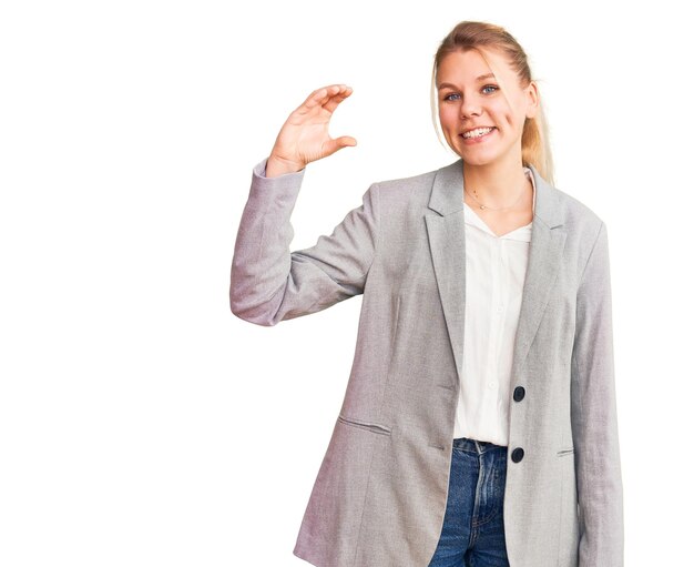 Joven hermosa mujer rubia con chaqueta elegante sonriendo y confiada gesticulando con la mano haciendo un signo de tamaño pequeño con los dedos mirando y la cámara. concepto de medida.