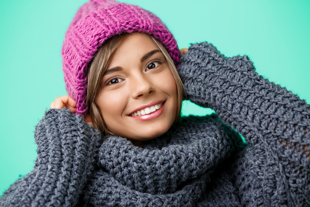 Joven hermosa mujer rubia en sombrero de punto y suéter sonriendo en verde.