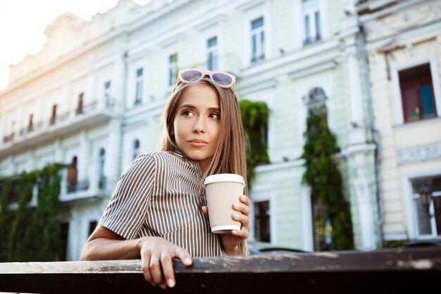 Joven hermosa mujer sentada en un banco, sosteniendo café